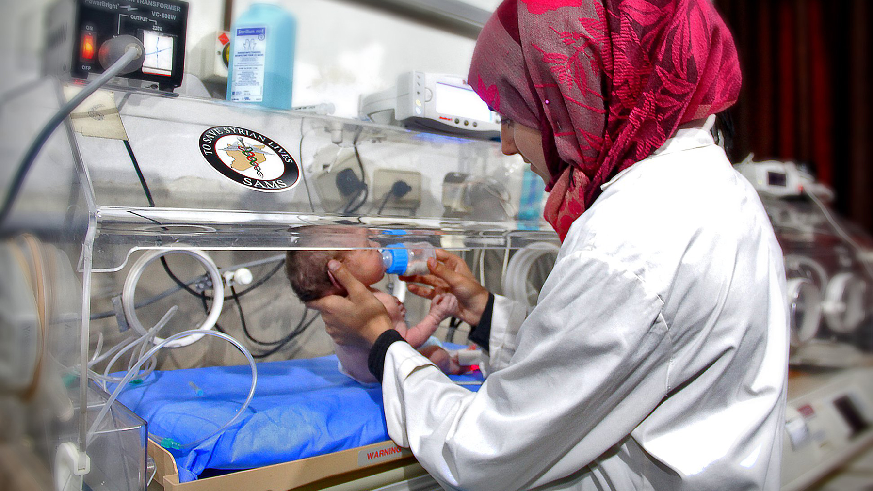 A health worker feeds a young infant in Syria. Babies whose mothers experience the physiological impacts of disaster may be more prone to lower birth weights and other health issues. (Photo courtesy of the Syrian American Medical Society)