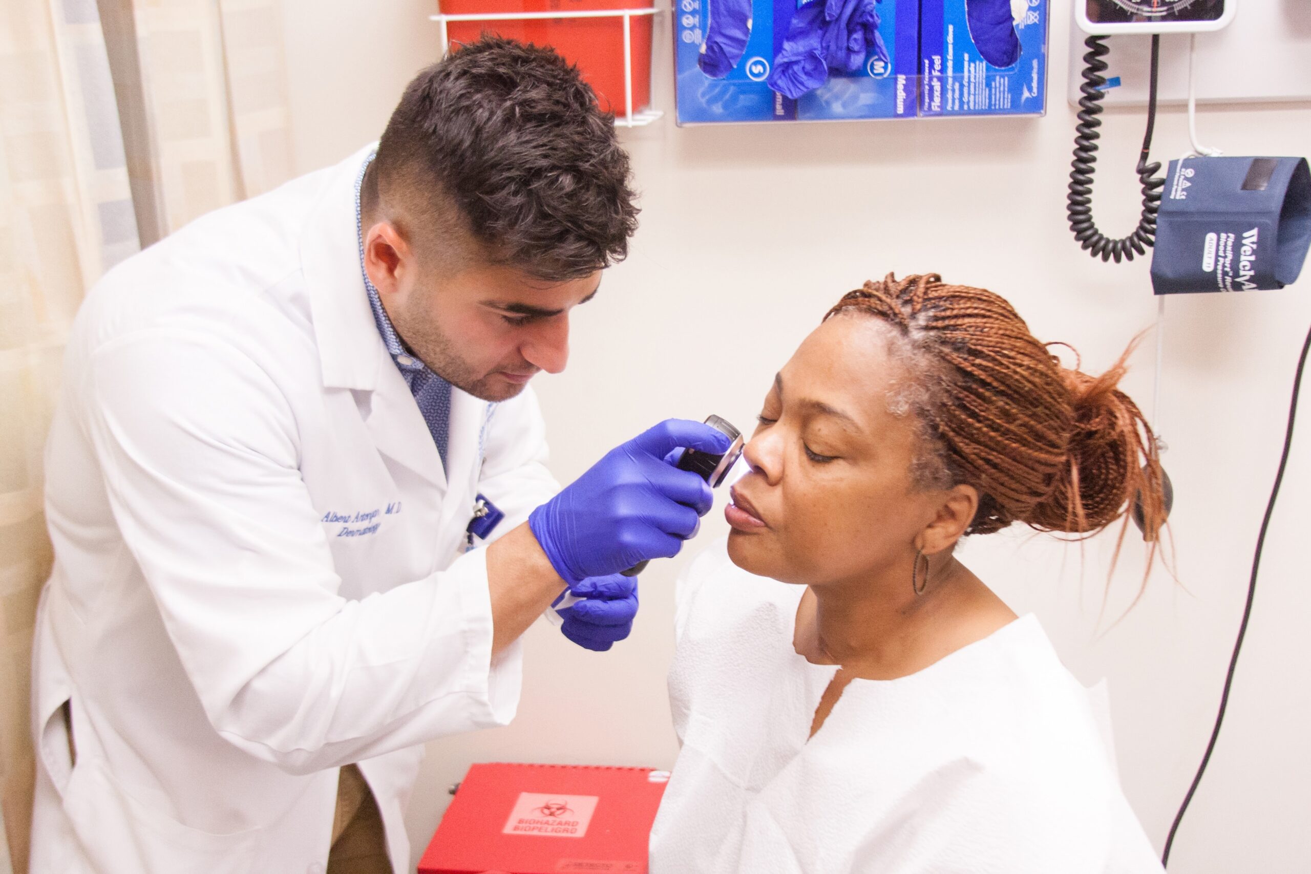 MD Resident Albert Antonyan conducts a skin screening for patient Tandra Tinsley at the Community Health and Social Services Center, Inc., known as CHASS, in Detroit last month as part of a community skin health event sponsored by the Vaseline Healing Project.(Photo by Stephanie Parshall for Direct Relief)