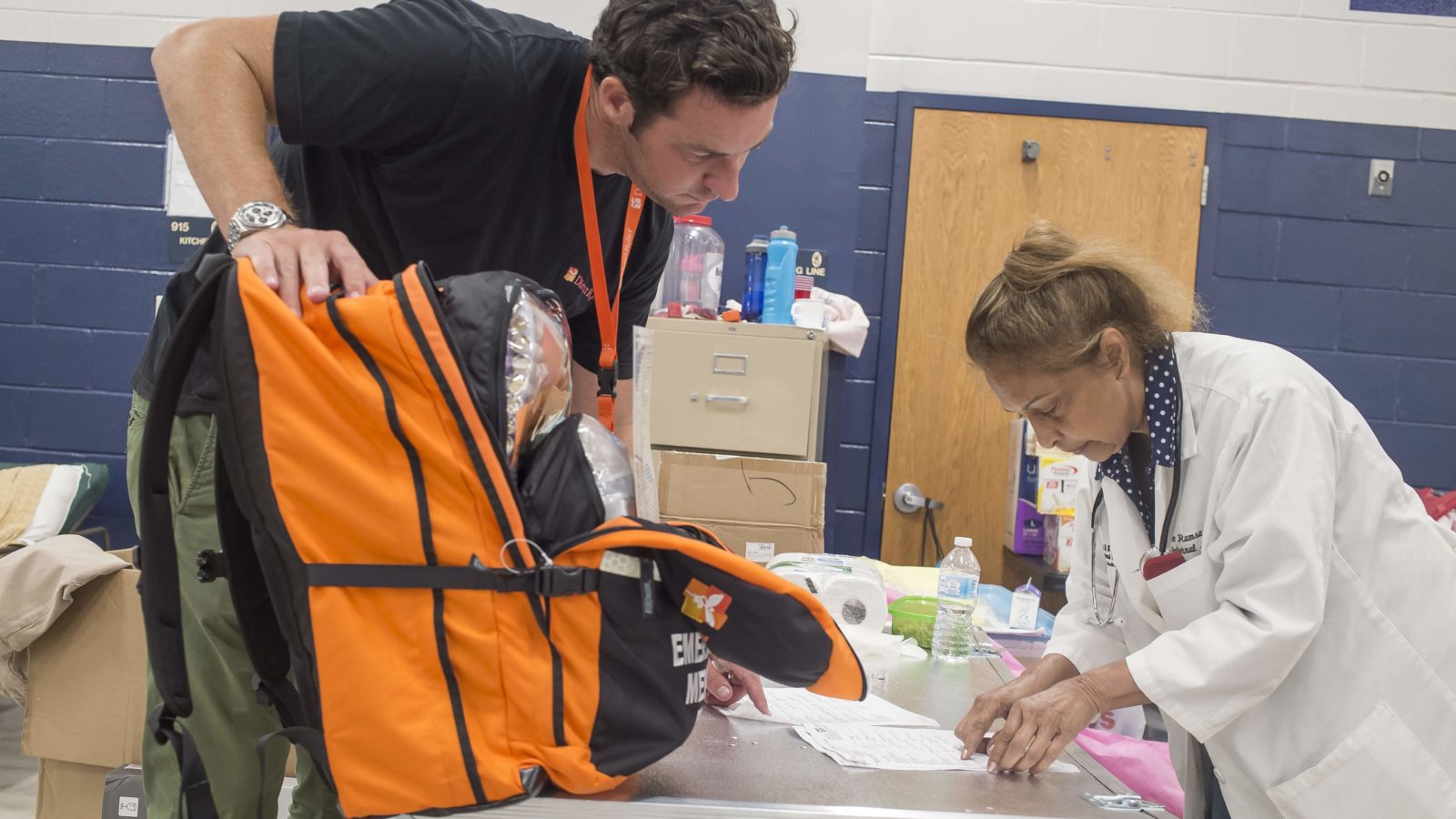 Direct Relief's Andrew MacCalla hands off an emergency medical backpack to Dr. Eileen Ramsaran, who was conducting medical care at a hurricane shelter in Panama City on Saturday, October 13, 2018.  The shelter was filled with medically vulnerable people who had been evacuated from local hospitals. (Photo by Zack Wittman for Direct Relief)